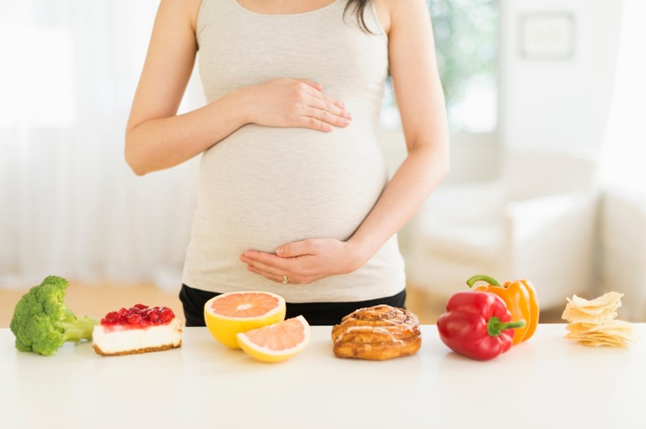 Mujer tocando su vientre, con alimentos saludables. Alimentos que contienen ácido fólico