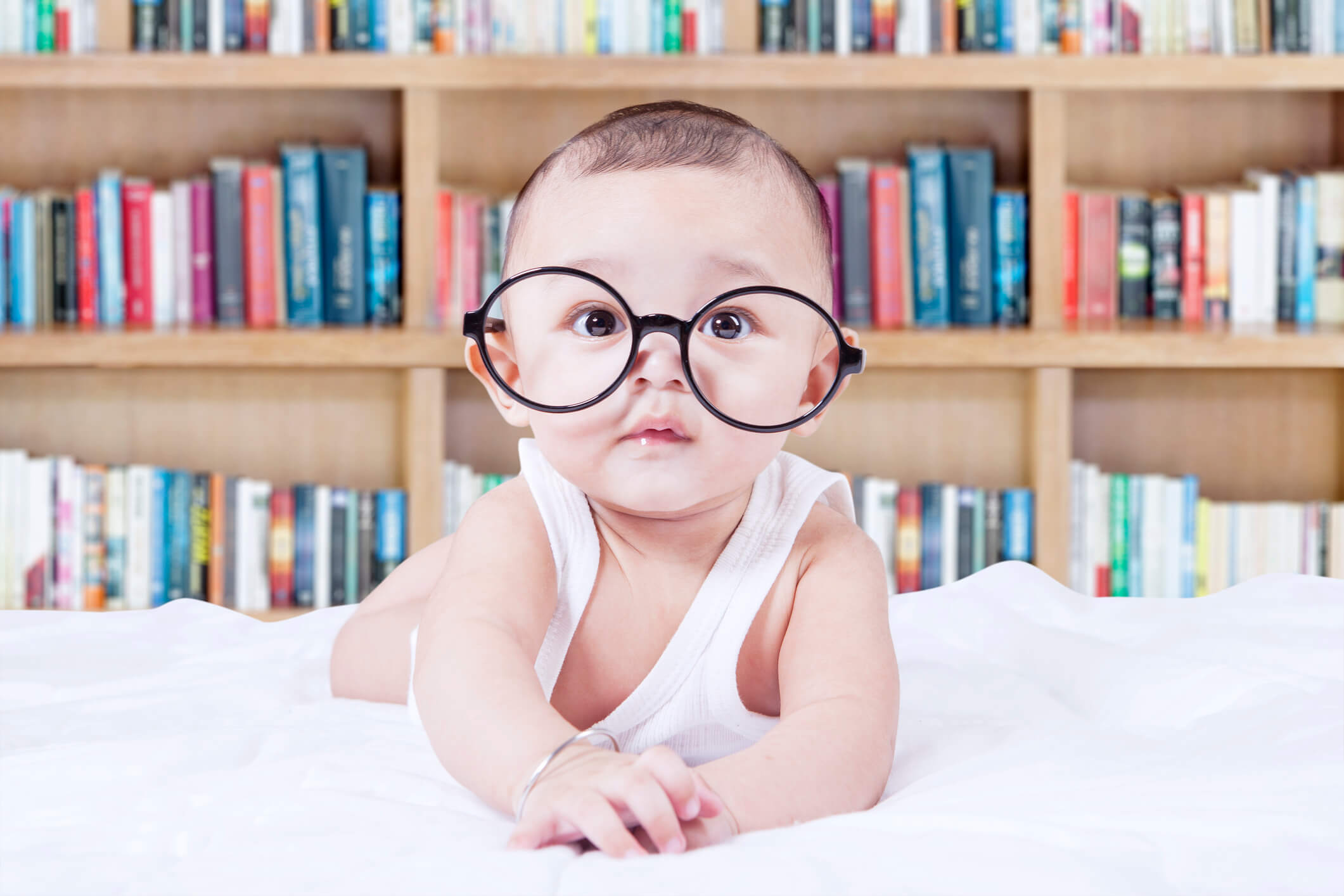 Bebé con lentes sobre una cama con fondo de librero
