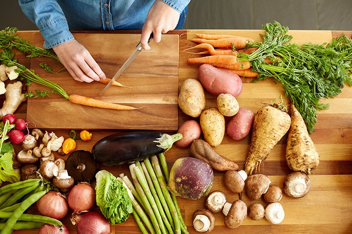 Mujer cortando verduras en la cocina sobre una tabla de madera creando hábitos saludables