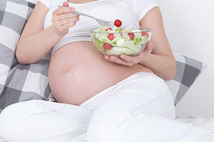 Joven embarazada comiendo una ensalada para prevenir el reflujo en el embarazo