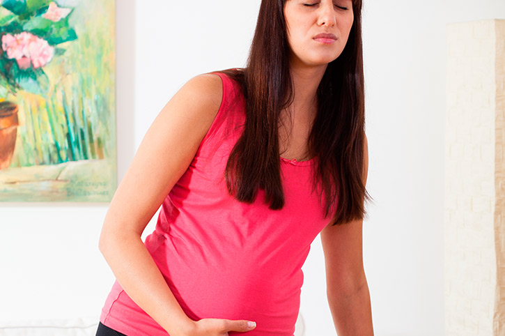 Mamá embarazada tocando su pancita de dolor debe evitar dormir después de comer
