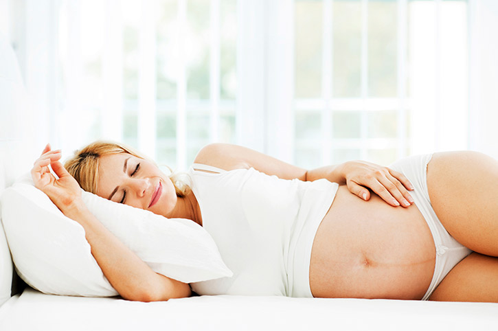 Mujer embarazada recostada en la cama usa almohadas para descansar mejor y tener su cabeza levantada