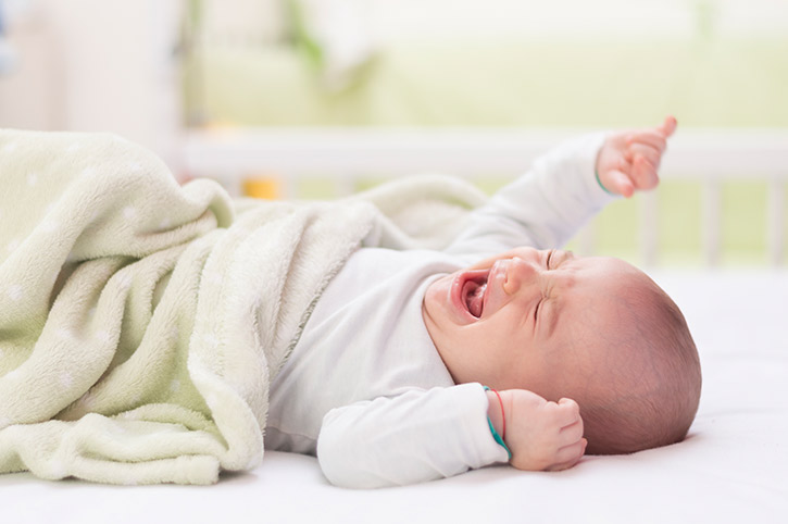 Niño con frazada verde llorando sobre la cama por síntomas de fiebre