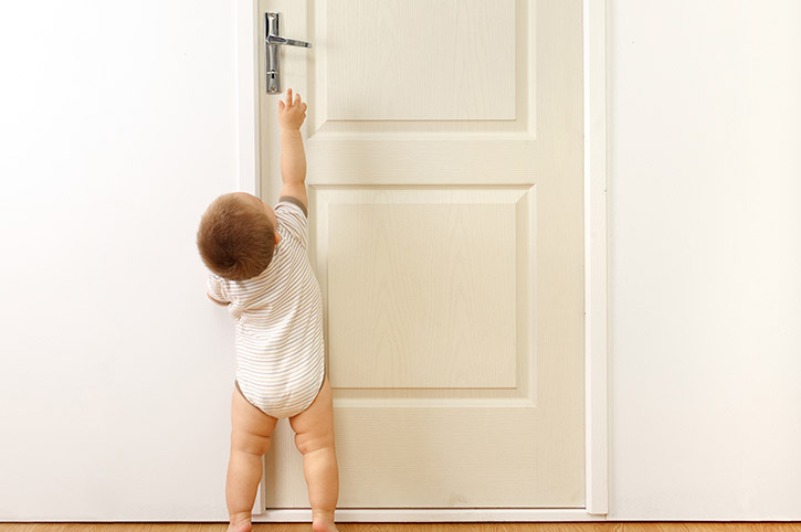 un bebé buscando alcanzar la manija de la puerta