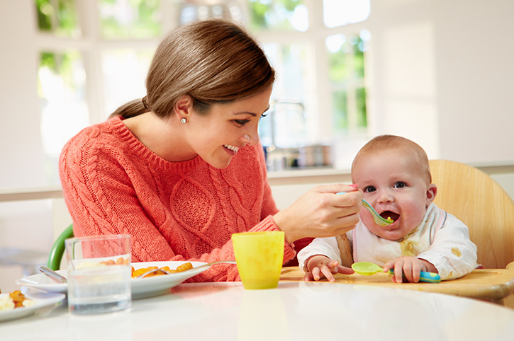 Madre alimentando con cuchara a su bebe con alimentos sólidos