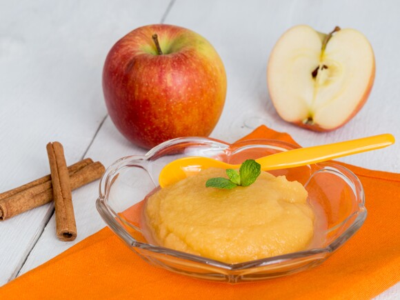 Papilla de manzana y canela en plato de cristal con una cuchara amarilla