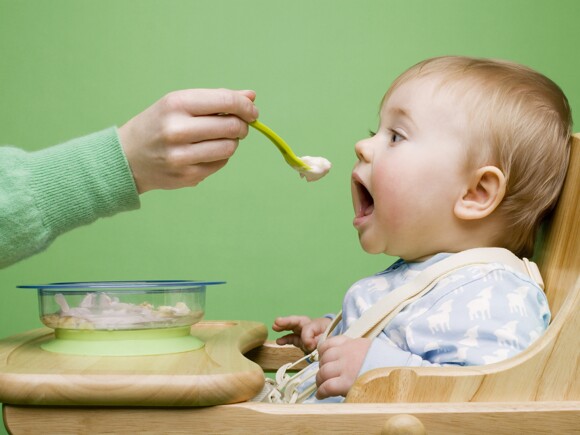 Bebé de un año sentado en una periquera a punto de comer de una cuchara