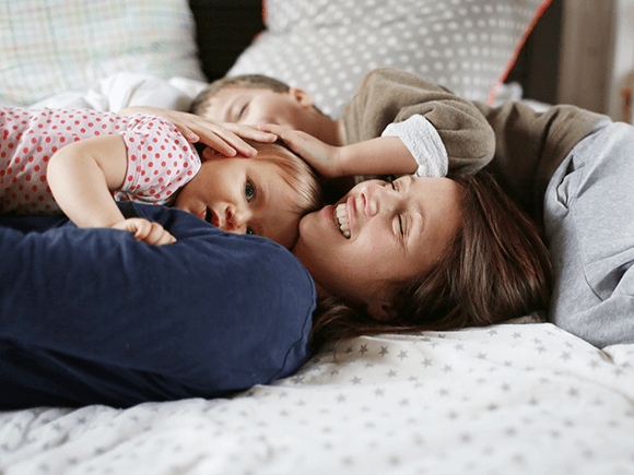 Una mujer y dos niños felices acostados en una cama.