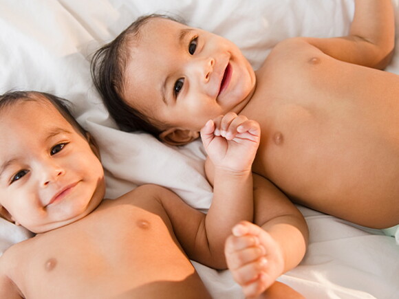 Bebés gemelos sonriendo acostados en la cama.