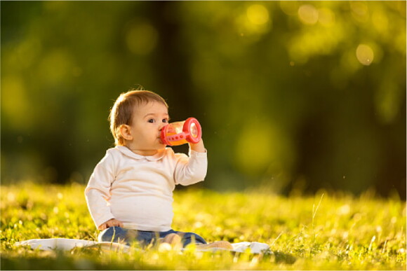 Niño sentado en el pasto tomando jugo hidratante 