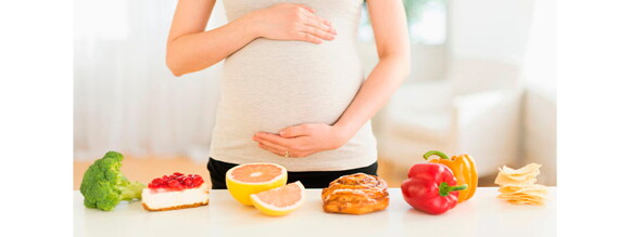 Mujer embarazada con una mesa de alimentos variados al frente 