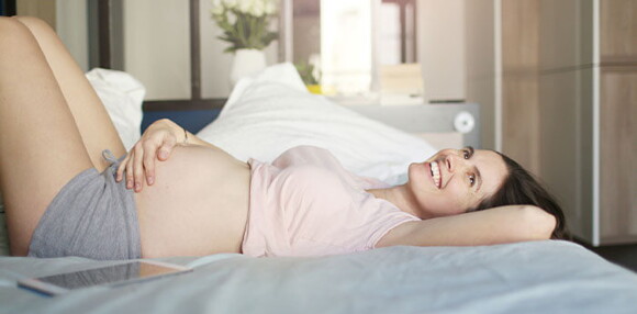 Mujer embarazada sonriendo acostada en la cama tocando su vientre.